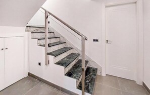 Una escalera con escalones de mármol y barandilla metálica que lleva a una puerta blanca.