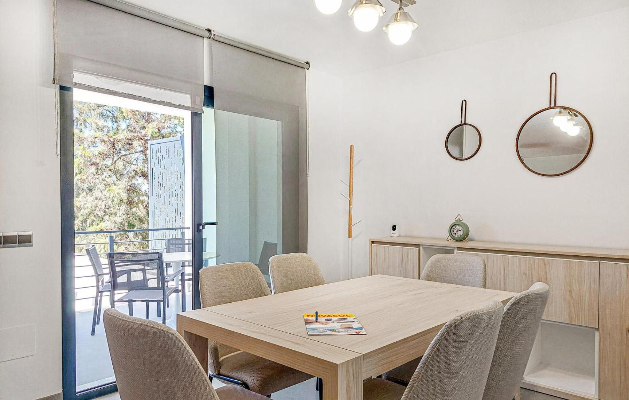 Un comedor moderno con una mesa y sillas de madera, un reloj pequeño y vistas al exterior a través de un ventanal.