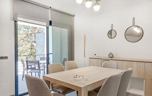 A modern dining area with a wooden table and chairs, a small clock, and a view of the outdoors through a glass door.