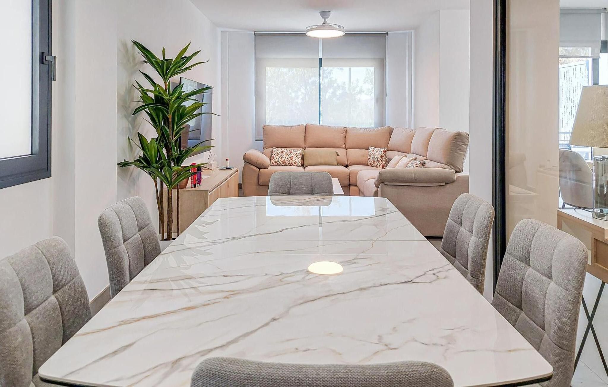 Una sala de estar moderna con un sofá color beige, un ventanal grande y una mesa de mármol.