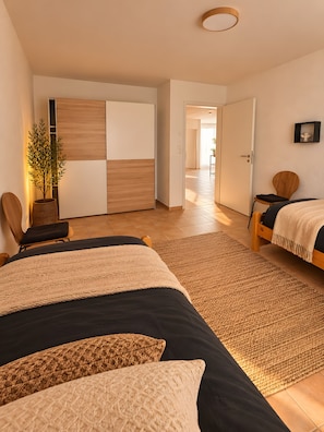 Een moderne slaapkamer met twee bedden, een groot raam en uitzicht op een gang.