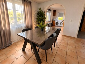 Een eethoek met een tafel, stoelen, een bloempot en uitzicht op een wasserij.