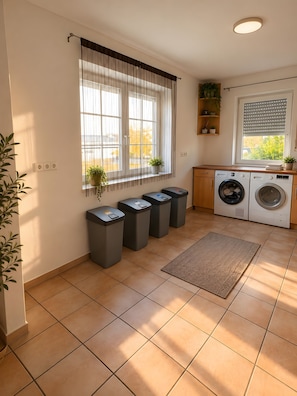 Een wasserette met een wasmachine, een droger en vier vuilnisbakken.
