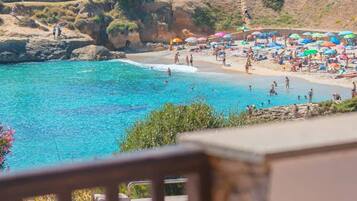 Vista sulla costa con spiaggia, acqua cristallina e un'area di parcheggio sullo sfondo.