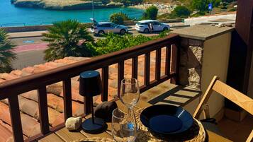 Un balcone con un tavolo apparecchiato per due, con vista su una zona costiera, auto parcheggiate e il mare.