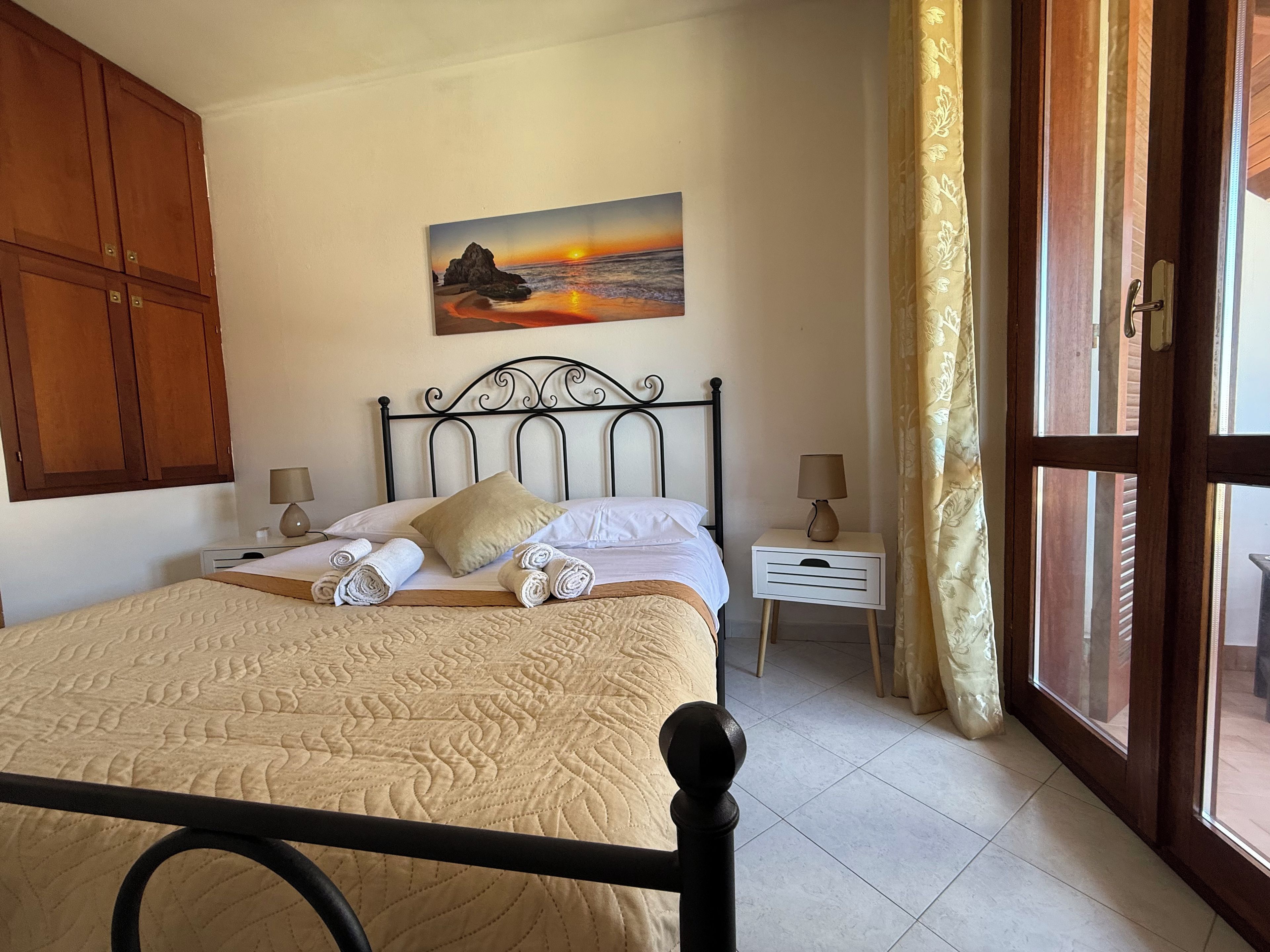 Una camera da letto con un letto, un quadro raffigurante un tramonto, un comodino e una finestra con tende.