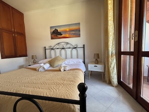 Een slaapkamer met een bed, een schilderij van een zonsondergang, een nachtkastje en een raam met gordijnen.