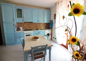 Een keuken met lichtblauwe kastjes, een eettafel met stoelen en een vaas met zonnebloemen.