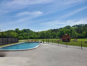 Una piscina con un deck cercado, un tobogán y una zona de juegos.