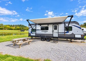 Una caravana Prowler con un toldo cubierto, una mesa de picnic y suelo de grava.