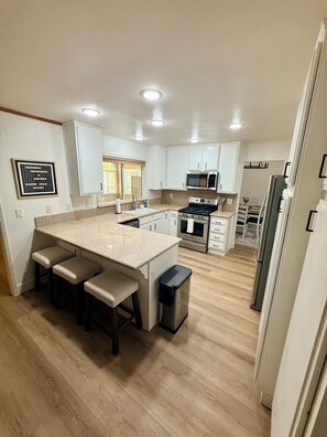 Una cocina moderna con armarios blancos, una isla central con taburetes y un refrigerador de acero inoxidable, además de un microondas.