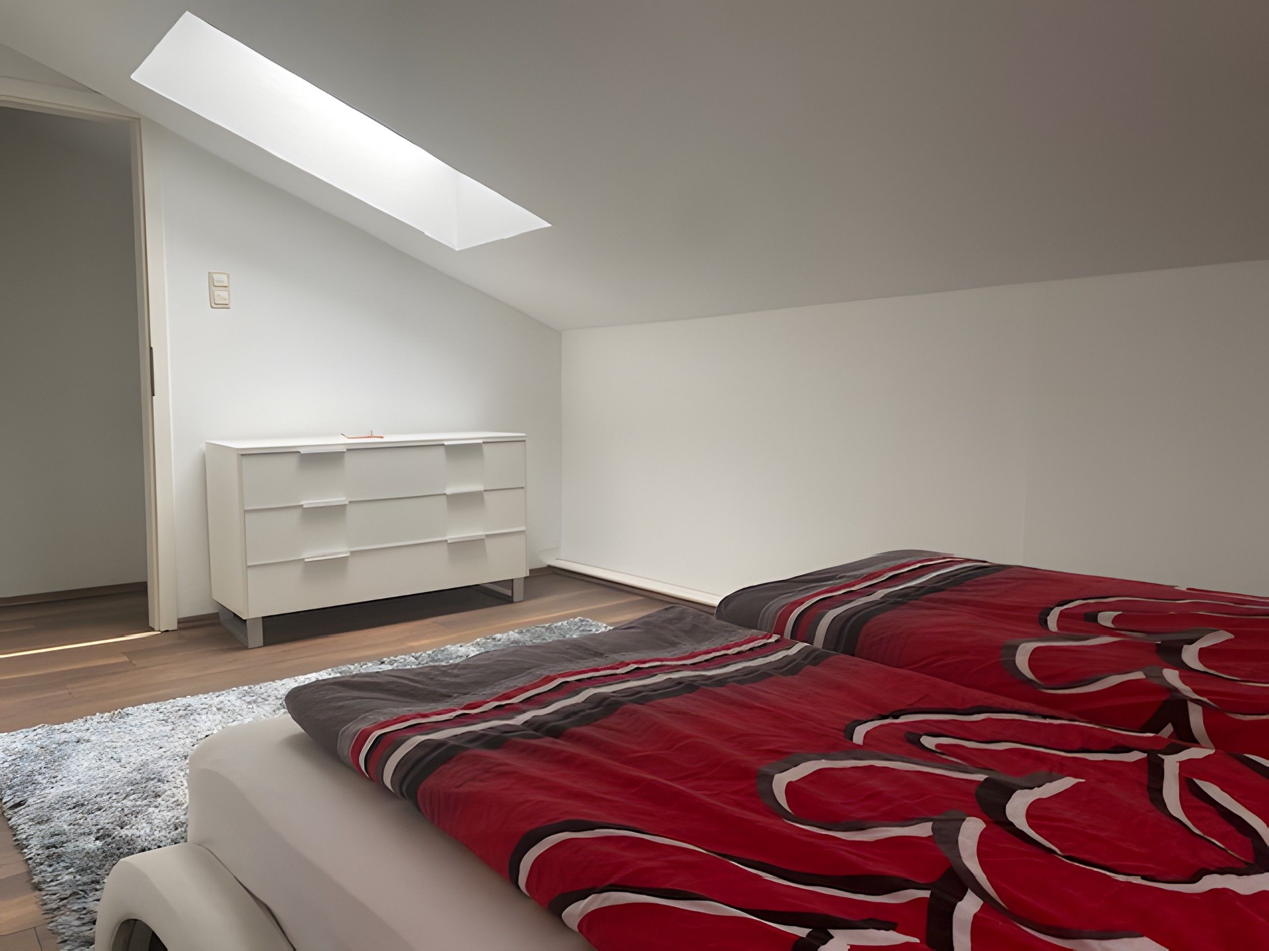 Ein Schlafzimmer mit einem Bett, einer weißen Kommode und einem Oberlicht.