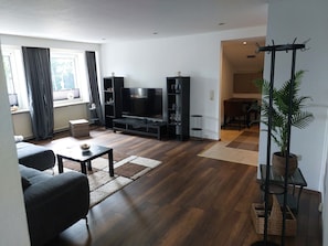 Ein modernes Wohnzimmer mit Flachbildfernseher, dunklen Möbeln und einem großen Fenster mit Vorhängen.