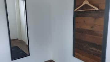 Un pasillo con suelo de madera, un tapete negro, un espejo y un panel de pared de madera con un colgador de madera.