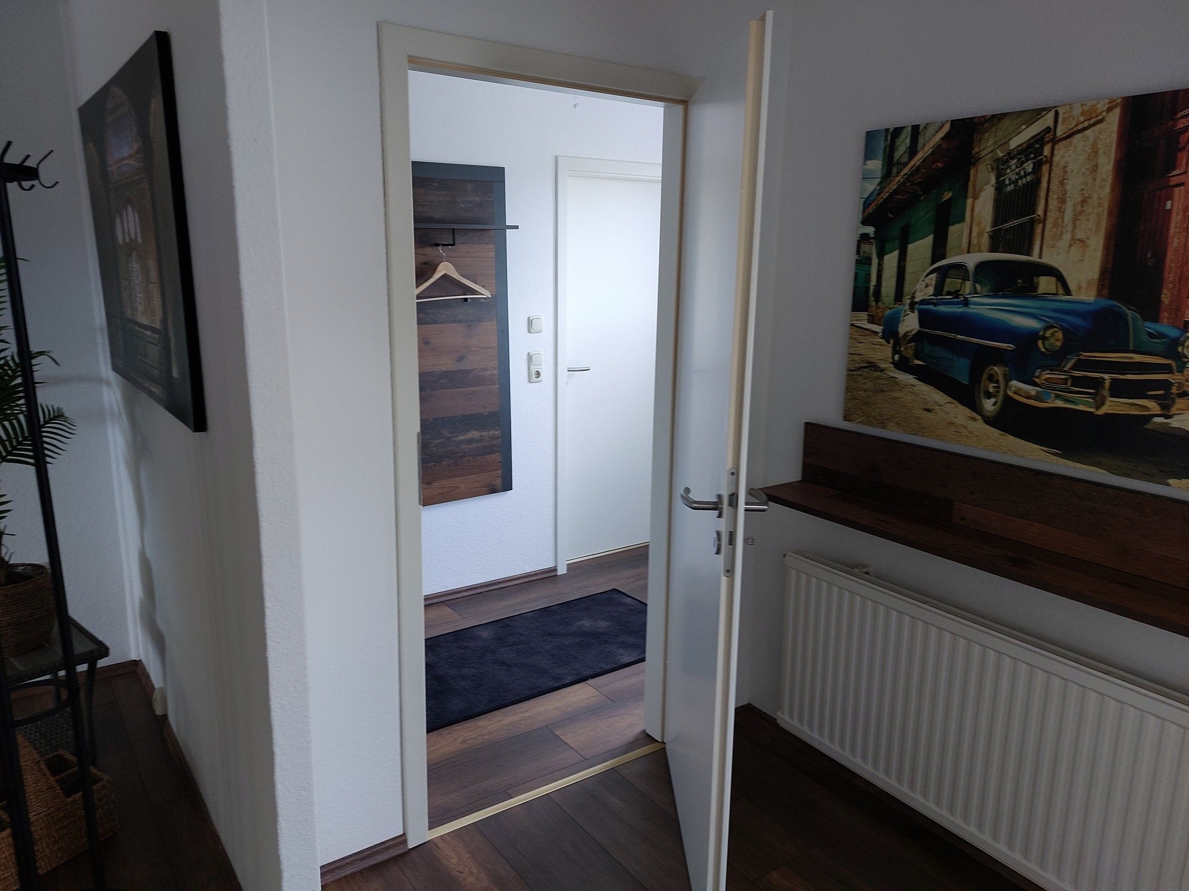 Ein Flur mit einer weißen Tür, Holzboden, einem Heizkörper und einem Bild von einem Auto an der Wand.