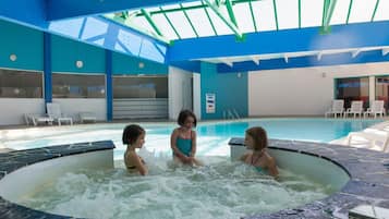 An indoor swimming pool with a tiled edge, a hot tub area, and lounge chairs.