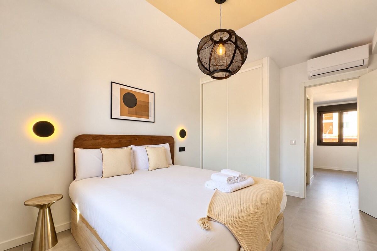 Une chambre à coucher moderne avec un grand lit, des lampes de chevet, un luminaire au plafond et une œuvre d’art encadrée accrochée au mur.