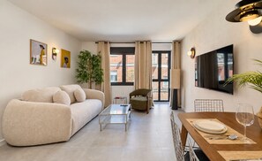 Un salon moderne avec un canapé, une table basse, une table à manger pour deux personnes et un téléviseur fixé au mur.