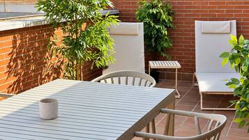 Un patio al aire libre con una mesa y sillas, rodeado de plantas en macetas y un muro de ladrillo.