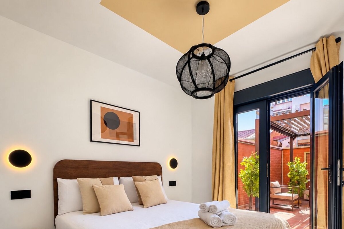 Une chambre moderne avec un grand lit, une table de chevet, une lampe fixée au mur et une vue sur l’extérieur.