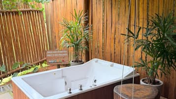 Een houten terras met een jacuzzi, potplanten en een houten omheining.