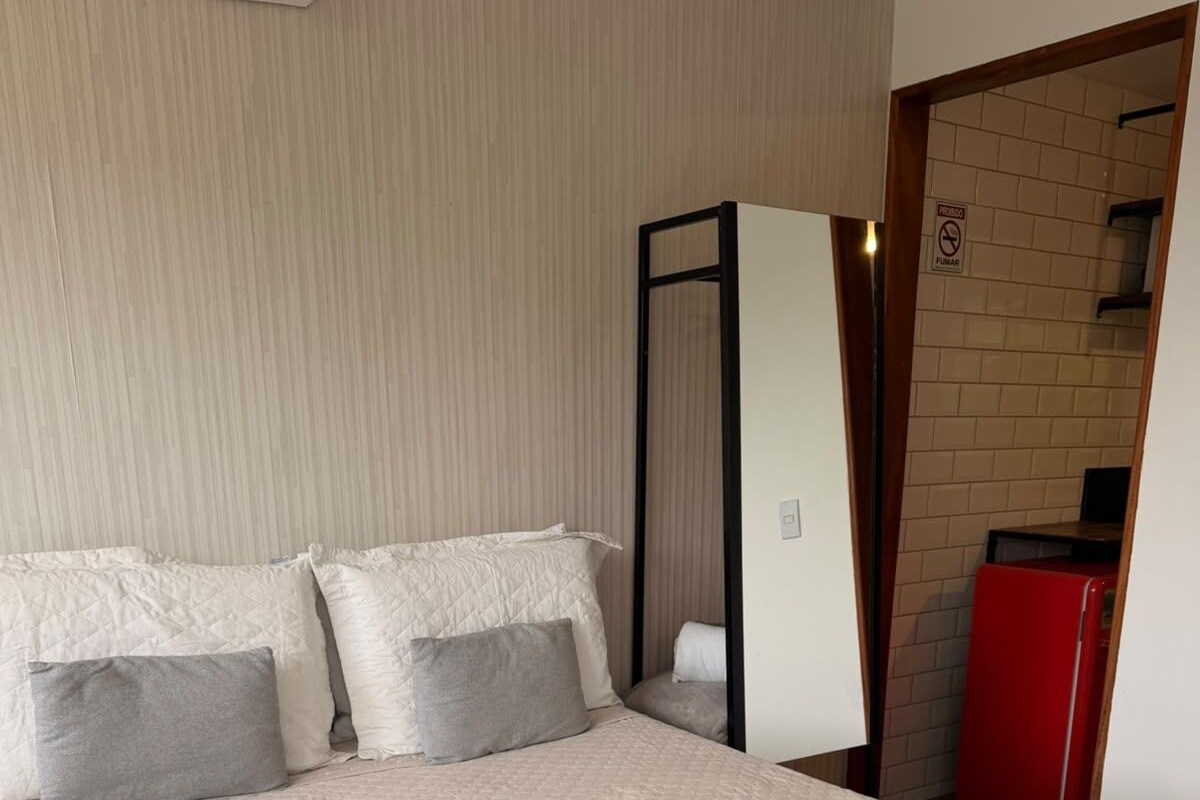 A hotel room with a bed, pillows, a red refrigerator, and a mirror.