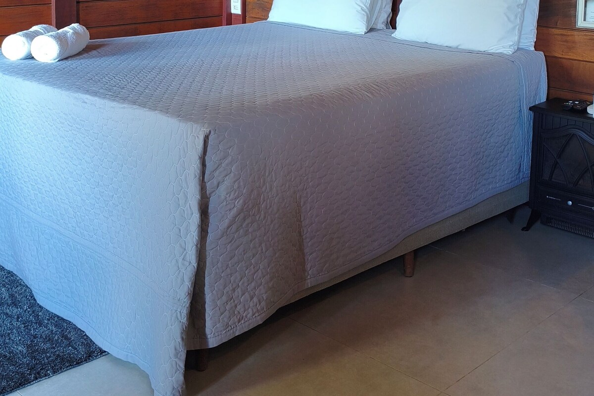 A single-bed room with a wooden headboard, a quilted bedspread, and a pair of white towels on the bed.