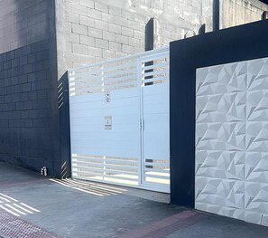 A gated entrance with a metal gate and a white wall with a geometric pattern. - New Listing (Vila Velha)