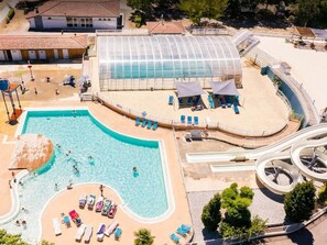 Vue aérienne d’un complexe hôtelier doté d’une grande piscine, d’un espace couvert et d’un toboggan aquatique.