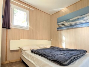 A bedroom with a bed, a window with curtains, and a painting of a seascape on the wall. - Chalet, pets welcome, AC - 7 guests (Soustons)