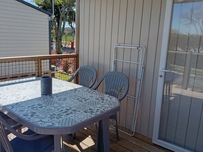 An outdoor patio with a table and two chairs, a metal gate, and a view of a garden. - Air-conditioned mobile home - 4 guests (Anduze)
