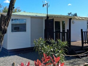 A single-story mobile home with a green roof, a small porch with a black railing, and a gravel driveway. - Air-conditioned mobile home - 4 guests (Anduze)