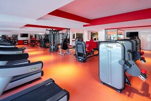 Un gimnasio moderno con equipo cardiovascular, máquinas de pesas y una decoración en colores rojo y blanco.