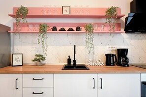 Eine Küche mit Marmor-Spritzschutz, einem Spülbecken, einer Kaffeemaschine und einem Regal mit Pflanzen und Gläsern.