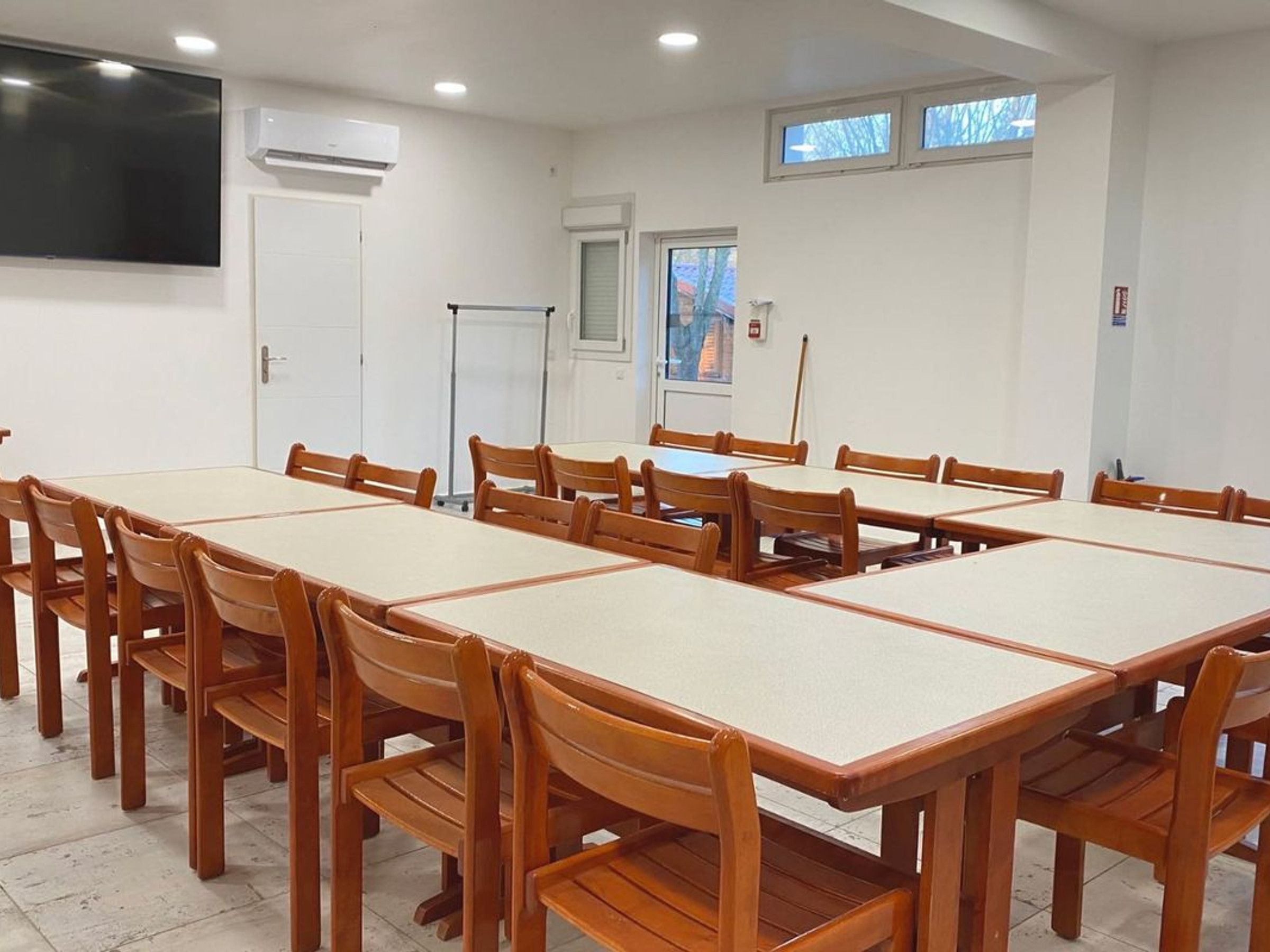 A conference room with a long table and chairs, white walls, and a large flat-screen TV.
