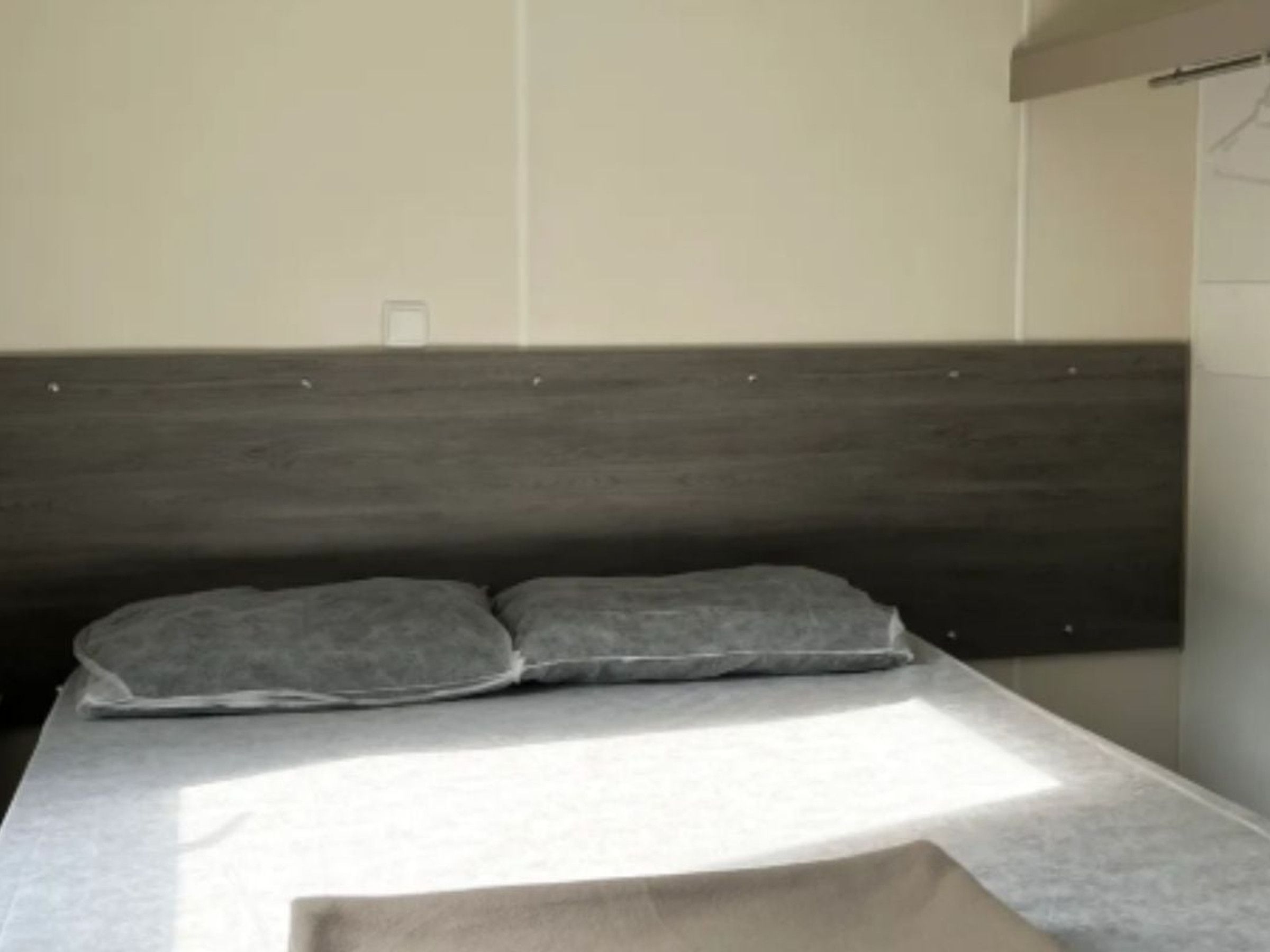 A bed with a dark headboard and two pillows, a white mattress, and a light-colored blanket.