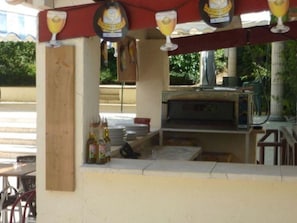 An outdoor bar area with a grill, stacked plates, and bottles.