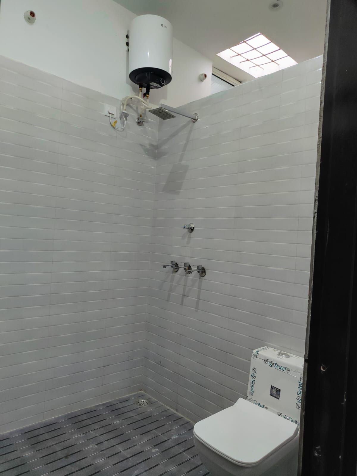 Casa de banho com paredes revestidas a azulejos brancos, sanita branca, chuveiro com unidade de teto branca e um claraboia.