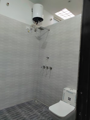 Casa de banho com paredes revestidas a azulejos brancos, sanita branca, chuveiro com unidade de teto branca e um claraboia.