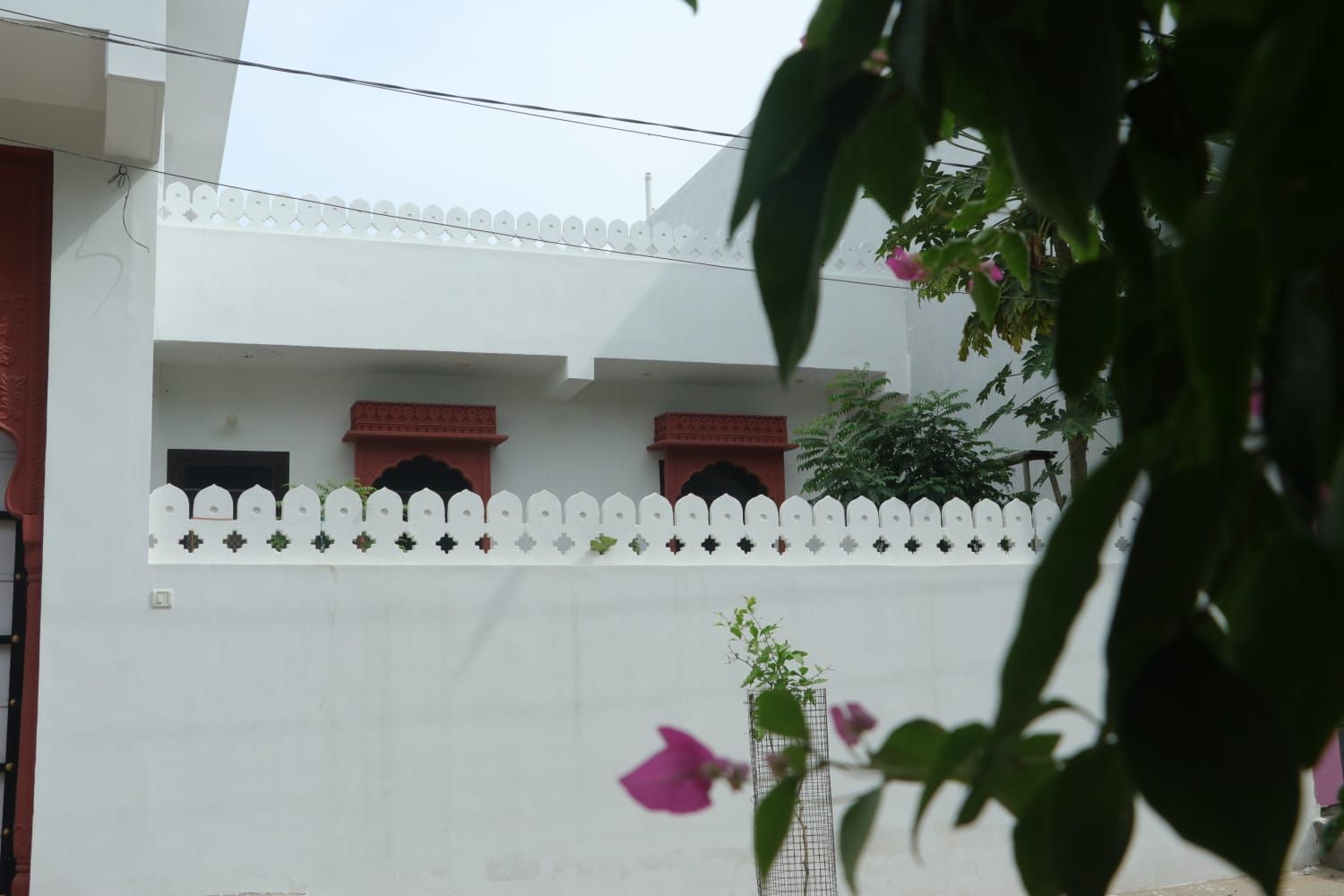 Um edifício branco com cerca branca de piquete e duas janelas com moldura vermelha.