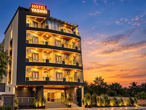 Un hotel de varios pisos con balcones, unidades de aire acondicionado y un cartel que indica el nombre 'HOTEL YASHVI'.