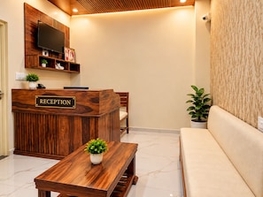 Un área de recepción con un mostrador de madera, un televisor de pantalla plana montado encima y un piso de baldosas de mármol.