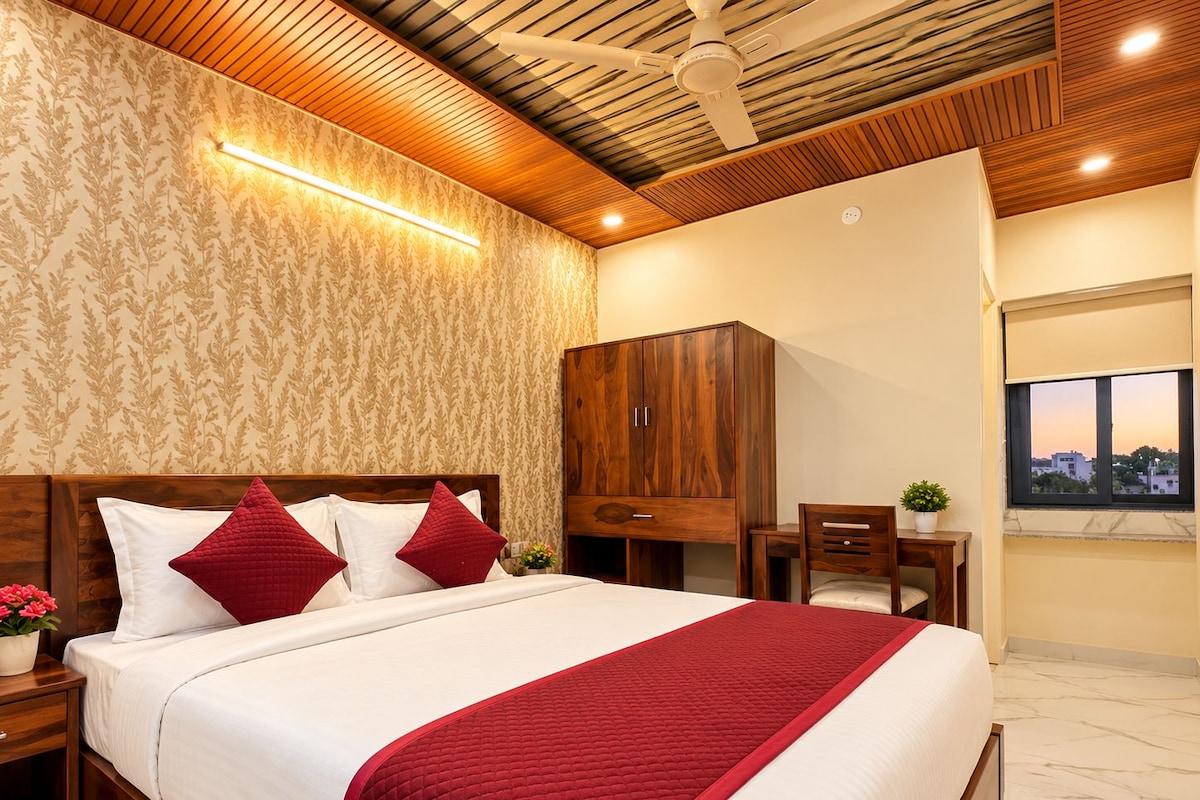 Habitación de hotel con cama, cabecero de madera, armario, escritorio, silla, ventana con vistas y ventilador de techo.
