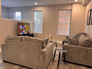 Una sala de estar con un televisor de pantalla plana grande, dos sofás, una mesa de centro de vidrio y un jarrón decorativo.
