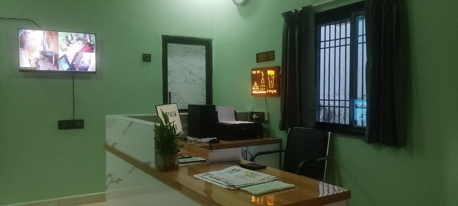 A reception area with a desk, a computer, a plant, and a wall-mounted television.