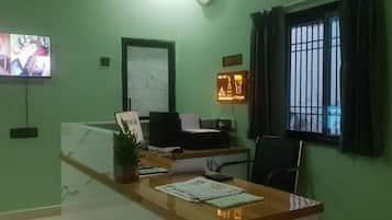 A reception area with a desk, a computer, a plant, and a wall-mounted television.