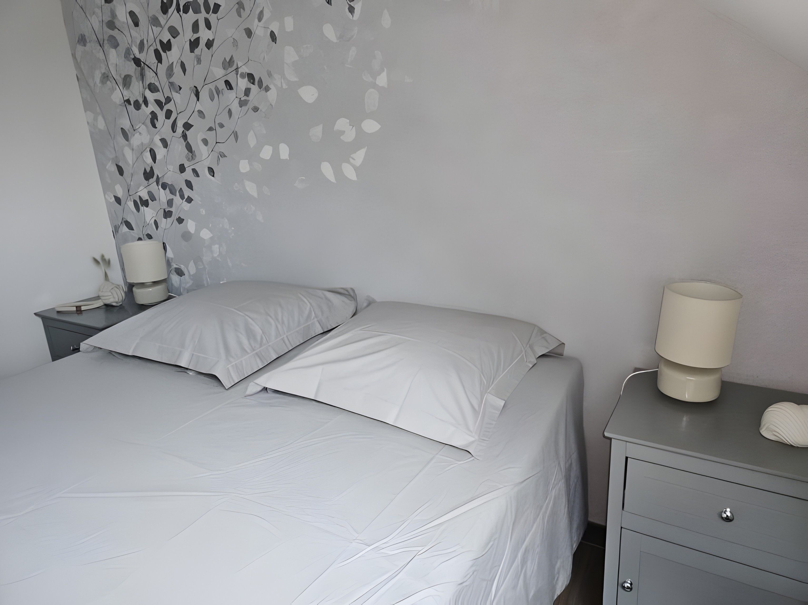 A neatly made bed with white bedding, a bedside lamp, and a wall with a leaf pattern.