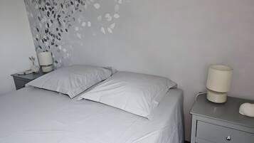 A neatly made bed with white bedding, a bedside lamp, and a wall with a leaf pattern.