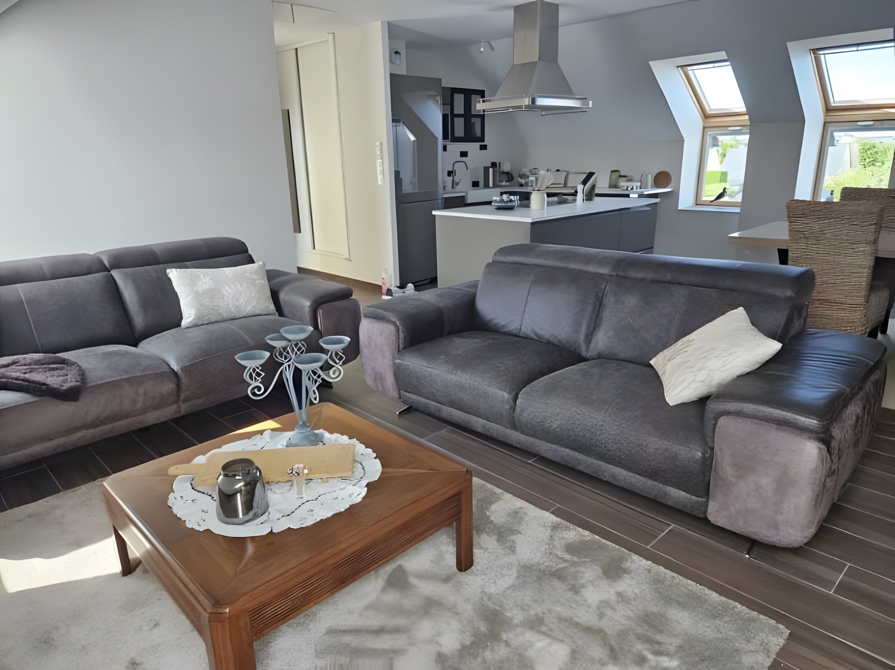 Een moderne woonkamer met twee grijze banken, een houten salontafel en een keuken op de achtergrond.