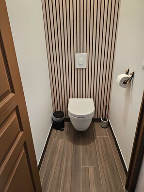 Un baño moderno con inodoro, un cesto de basura y un dispensador de papel higiénico.